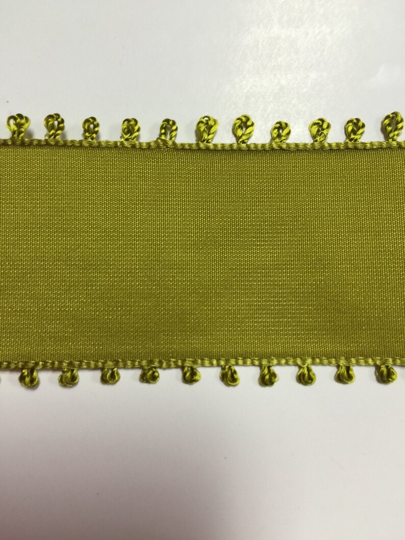 May include: A green ribbon with a decorative edge of small green loops. The ribbon is smooth and has a subtle sheen.