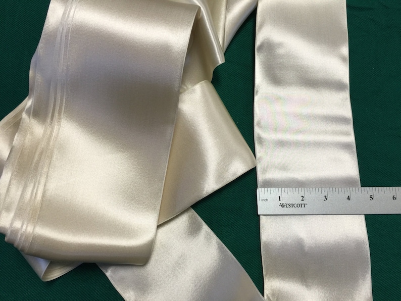 May include: A roll of ivory satin ribbon with a double-stitched edge. The ribbon is 6 inches wide and is measured with a ruler.