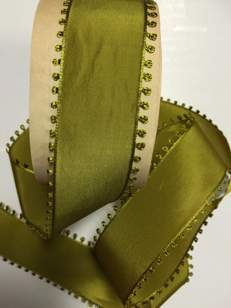 May include: Olive green satin ribbon with a decorative beaded edge. The ribbon is rolled on a cardboard spool.