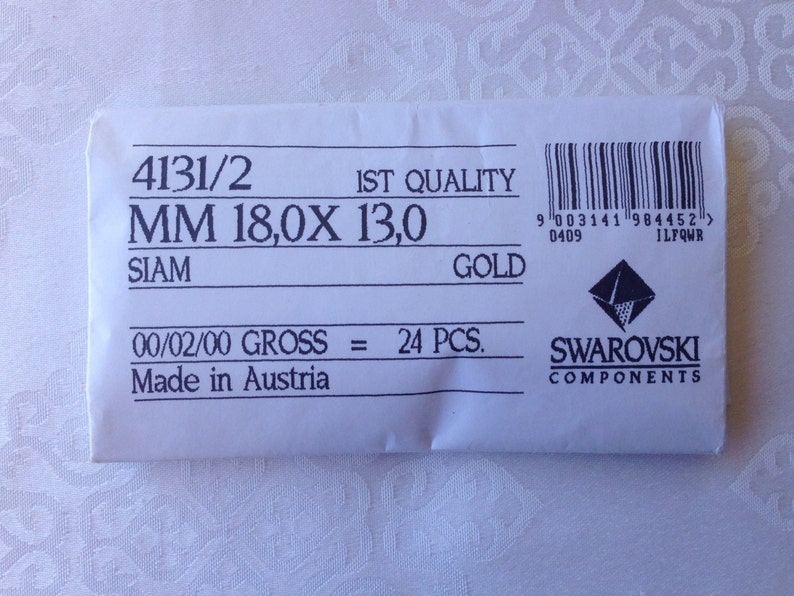 May include: A white paper bag with the text "4131/2 IST QUALITY MM 18,0X 13,0 SIAM GOLD 00/02/00 GROSS = 24 PCS. Made in Austria" and a Swarovski logo with the text "SWAROVSKI COMPONENTS".