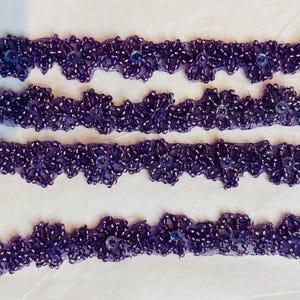 May include: Purple beaded trim with a scalloped edge. The trim is made of small beads sewn onto a sheer fabric.