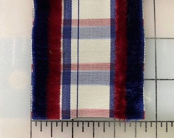 Può includere: Primo piano di un nastro a quadri bianco, blu e rosso con un bordo in velluto blu scuro su ogni lato. Il nastro è misurato su un righello, mostrando che è largo circa 5 cm.