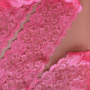May include: Pink lace trim with a floral pattern. The lace has a scalloped edge.