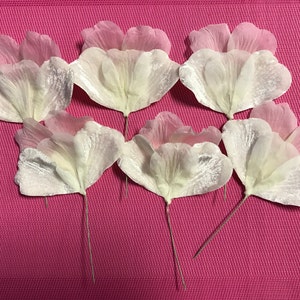 May include: Seven white and pink fabric flower petals with wire stems. The petals are layered and have a slightly iridescent sheen.