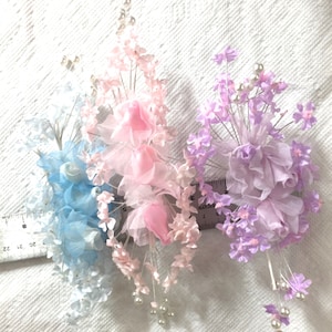 Könnte beinhalten: Drei Seidenblumenarrangements in Blau, Rosa und Lila mit Perlenakzenten. Jedes Arrangement hat eine Ansammlung von Blumen mit einer einzigen größeren Blume in der Mitte.