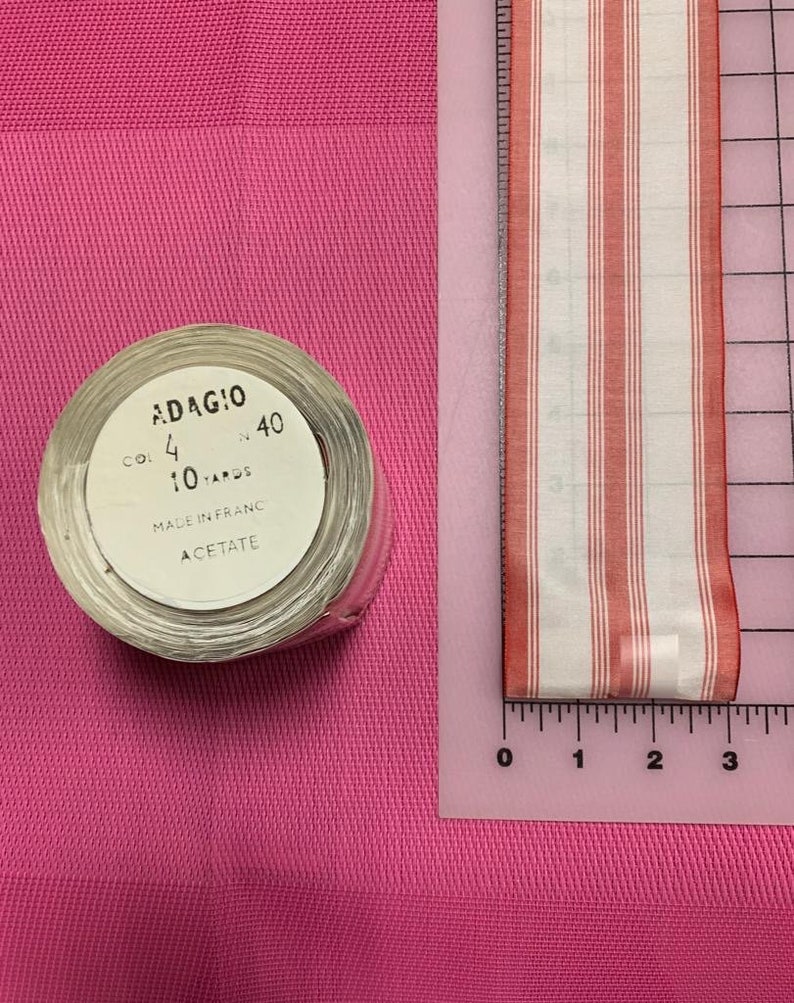 May include: A roll of red and white striped ribbon with a label that reads "ADAGIO CO! 4 40 10 YARDS MADE IN FRANC ACETATE".