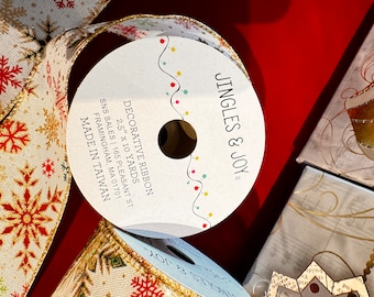 May include: A roll of 2.5 inch wide decorative ribbon with a snowflake pattern in red, gold, and white on a beige background. The ribbon is 10 yards long and is made in Taiwan. The label reads "Jingles & Joy" and "Decorative Ribbon 2.5" x 10 Yards".