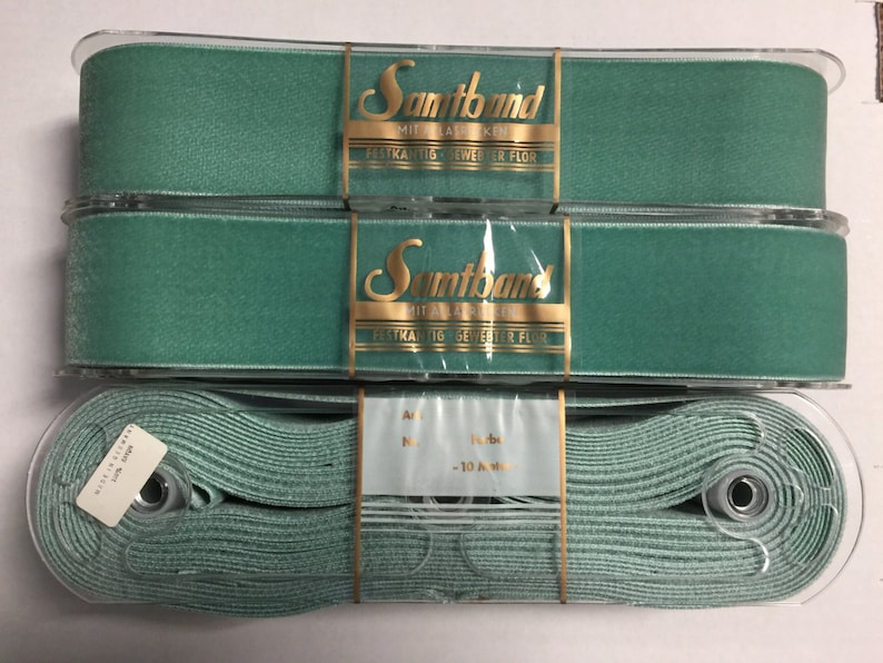 May include: Three spools of teal blue satin ribbon. The ribbon is packaged in clear plastic and labeled "Samband Mit Elastischen", "Festhaftende Seweher fur Flor".