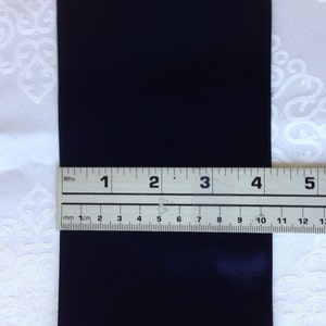 May include: A close-up of a black satin ribbon measured with a ruler. The ruler shows measurements in both inches and centimetres.