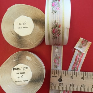 Könnte beinhalten: Zwei Spulen beigefarbenes Band mit Blumenmustern und goldenen Akzenten. Die Spulen sind mit dem Text "Col. 46 100% Rayon" und "Patt. 17875 10 Yards No. 5 Made in France" beschriftet. Ein Lineal aus Holz ist zur Skalierung enthalten.