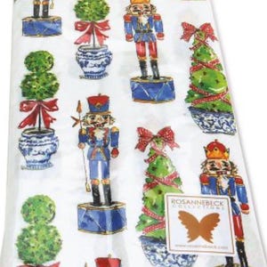 May include: White paper napkins with a repeating pattern of nutcrackers, topiary trees, and Christmas trees in blue, red, and green. The napkins have the text "thr SINCE 1977" and a "ROSANNEBECK COLLECTIONS" label.