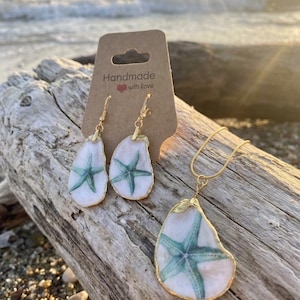 May include: A handmade jewelry set featuring a necklace and earrings. The earrings and pendant have a white background with a teal starfish design, edged in gold. The card reads "Handmade with love."