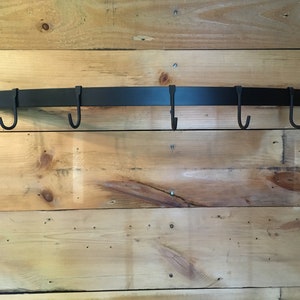 May include: Black metal pot rack with five hooks mounted on a wooden wall.