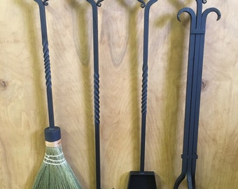 May include: A set of four black metal fireplace tools hanging on a wall-mounted rack. The tools include a poker, a shovel, a brush, and tongs. The tools are all made of wrought iron and have a rustic finish.