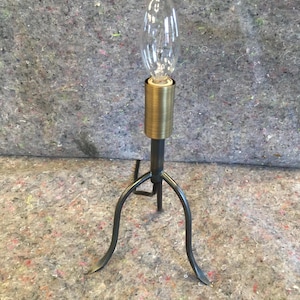 May include: A black metal table lamp with a gold-colored base and a clear teardrop-shaped light bulb.