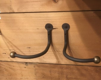May include: Two black metal hooks with rounded ends, mounted on a wooden wall. The hooks are curved and have a simple design.