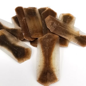 Puede incluir: Un grupo de cristales translúcidos marrones y blancos con una superficie rugosa y texturizada. Los cristales están dispuestos en una pila, con algunos superpuestos.