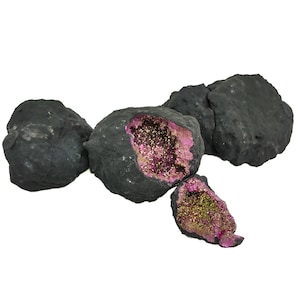 Könnte beinhalten: Vier schwarze Geodenkristalle mit rosafarbenen und goldenen Innenräumen. Die Kristalle sind zusammen gruppiert und einer ist aufgebrochen, um das funkelnde Innere zu zeigen.