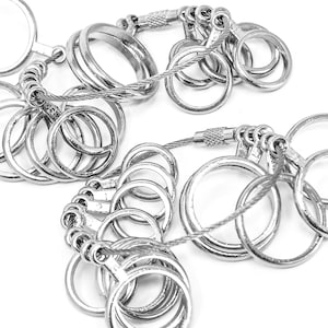 May include: Close-up of several silver keyrings with multiple rings attached to a flexible steel cable. The keyrings are arranged in a pattern, with varying sizes of rings.