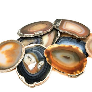 May include: A collection of agate slices in various shades of brown, white, and black. The slices are arranged in a pile, with some overlapping. The agate slices are smooth and polished, with a natural, organic look.