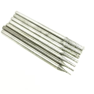 Puede incluir: Un juego de siete brocas de punta de diamante plateadas para usar en una herramienta rotativa. Las brocas son de diferentes tamaños y formas.