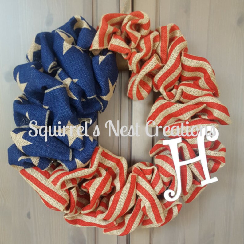 May include: A burlap wreath decorated with red, white, and blue burlap in the style of the American flag. The wreath has a white letter "H" attached to it. The wreath is hanging on a wooden door.
