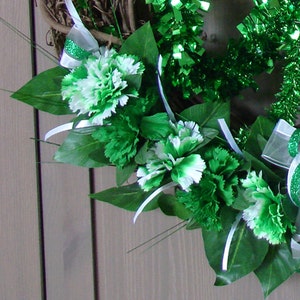May include: A green and white wreath with green and white carnations and green leaves. The wreath is decorated with green and white ribbon.