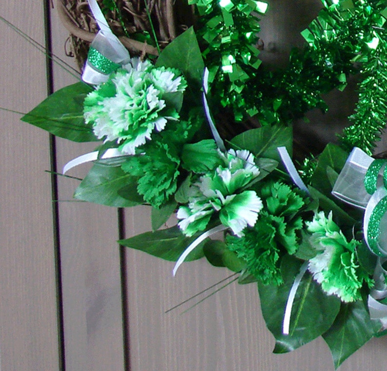 May include: A green and white wreath with green and white carnations and green leaves. The wreath is decorated with green and white ribbon.