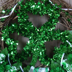 May include: A green shamrock-shaped wreath made of tinsel, with white ribbon and green carnations.