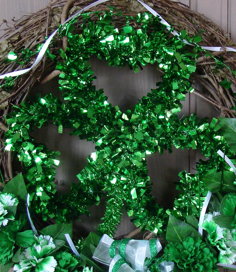 May include: A green shamrock-shaped wreath made of tinsel, with white ribbon and green carnations.