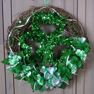 May include: A green shamrock wreath made of grapevine with green tinsel and white ribbon accents. The wreath is decorated with white and green carnations.