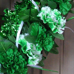 May include: A green and white floral wreath with green leaves and white ribbon. The wreath is decorated with green and white carnations.