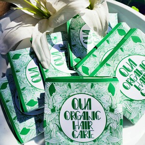 May include: A stack of green and white boxes with a floral pattern and the text "QUI ORGANIC HAIR CARE" on the top box.