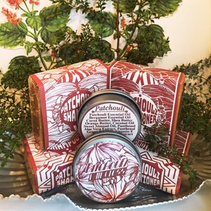 May include: Two round metal tins with red and white labels that say "Patchouli" and "Patchouli Conditioner". The tins are sitting on top of two brown bars of soap with red and white labels that say "Patchouli Shampoo".