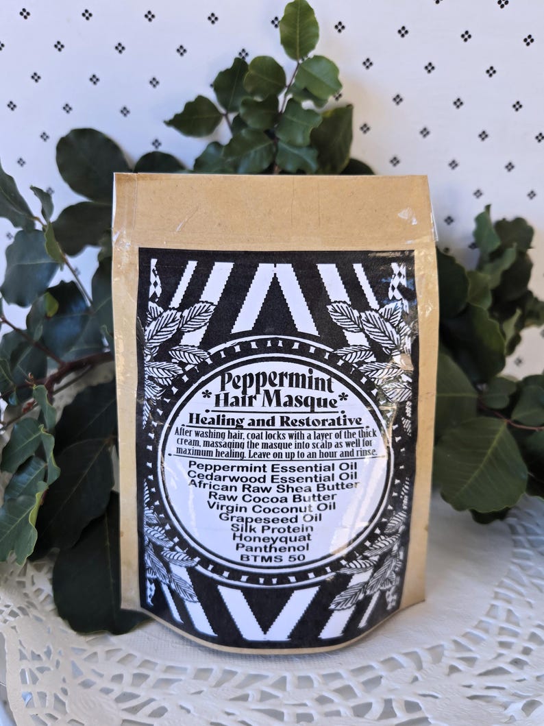 Op de afbeelding: Een bruine papieren zak met een zwart-wit etiket waarop "Peppermint Hair Masque" staat en de ingredi&euml;nten worden vermeld: pepermuntolie, cederhouten olie, Afrikaanse ruwe sheaboter, ruwe cacaoboter, virgin kokosolie, druivenpitolie, zijdeprote&iuml;ne, honingwas, panthenol, BTMS 50.