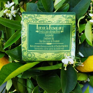 Puede incluir: Una barra de jab&oacute;n verde y blanca con el texto "Lemon & Rosemary Fresh & Light Silkening Blend Shampoo Bar Conditioner Bar Hair Gloss Leave-In Treatment Made with Lemon & Rosemary essential Oils. All Plant Based Ingredients Concentrated in a solid for superior, ultra healthy results" en la etiqueta. El jab&oacute;n est&aacute; rodeado de hojas verdes y limones amarillos.