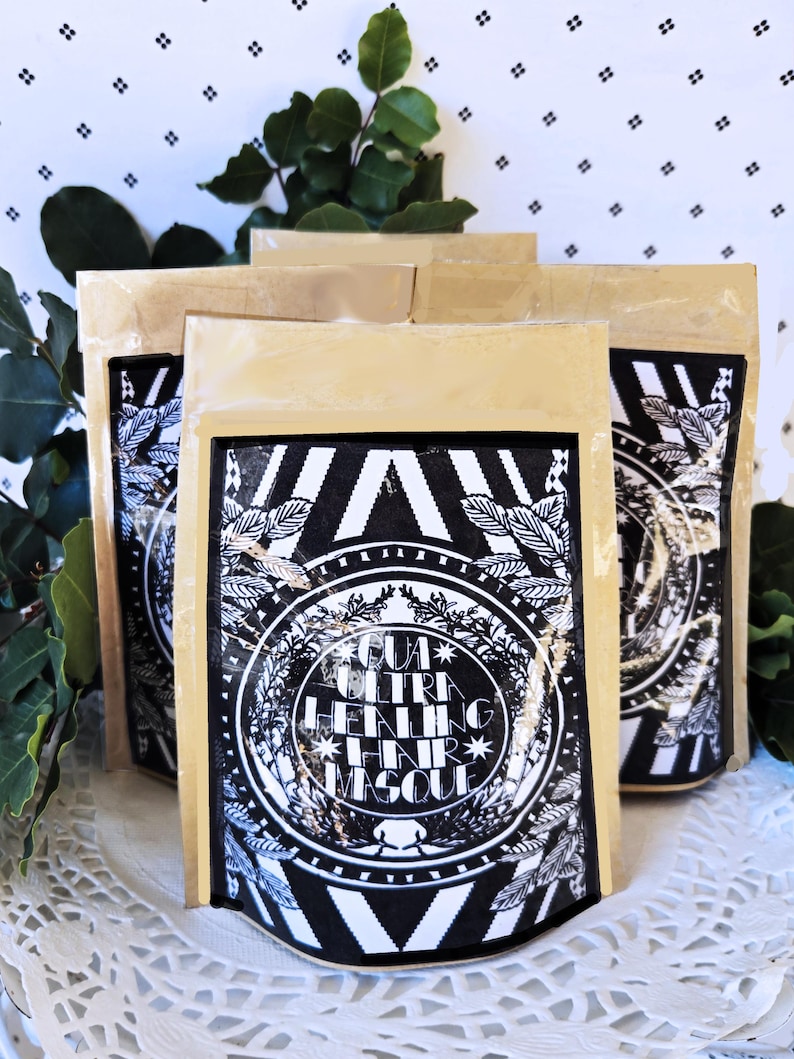 Op de afbeelding: Drie bruine papieren zakjes met zwarte en witte etiketten. Het etiket toont een zwart-witte illustratie van een bebladerde tak met de tekst "GUA ULTRA HEALING HAIR MASQUE".