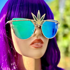 May include: A pair of blue mirrored sunglasses with a gold frame and a rhinestone-encrusted marijuana leaf design on the bridge.