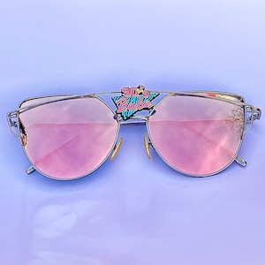 May include: Silver cat-eye sunglasses with pink mirrored lenses and a 90's Babe pin on the frame.
