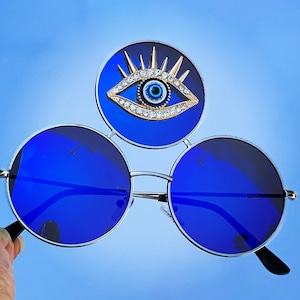 May include: Round blue sunglasses with a blue evil eye charm on the bridge of the nose.