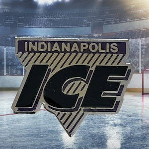 Puede incluir: Un pin plateado y negro de Indianapolis Ice. El pin presenta el nombre del equipo en letras plateadas sobre la palabra "ICE" en letras negras grandes. El pin tiene un borde púrpura y un diseño de rayas diagonales.