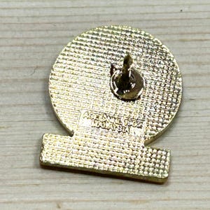 Puede incluir: Un pin dorado con una parte superior redonda y una inferior rectangular. El pin tiene una superficie texturizada y un cierre de alfiler. El texto "ACE SDN BHD MALAYSIA" es visible en el pin.