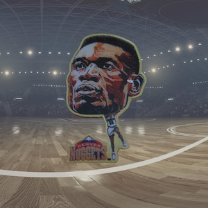 Può includere: Una carta da basket gialla e marrone con un'illustrazione a cartone animato di un giocatore di basket con la scritta "Denver Nuggets" sotto.