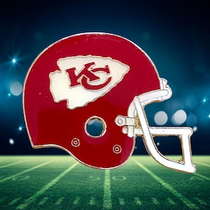 May include: A red and white football helmet pin featuring the Kansas City Chiefs logo. The helmet has a red shell with a white facemask and the team's logo prominently displayed on the side.