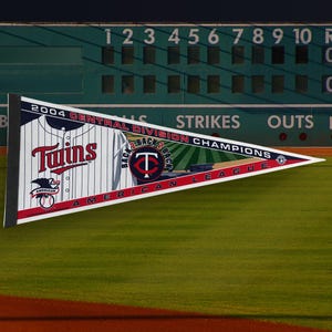 May include: A pennant flag featuring the Minnesota Twins logo and the text "2004 Central Division Champions Back 2 Back American League". The flag is white with red, blue, and gold accents.
