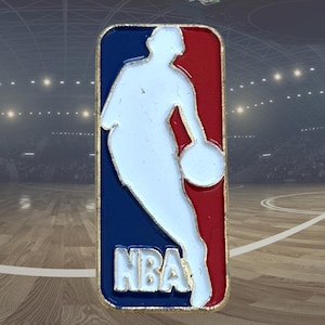 Op de afbeelding: Een rechthoekige pin met het NBA-logo. De pin heeft een gouden rand, met een wit silhouet van een basketballer in het midden. De achtergrond is verdeeld in rode en blauwe secties, met de letters "NBA" onderaan.