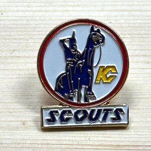 Puede incluir: Un pin vintage de los Scouts con borde dorado. El pin presenta un dise&ntilde;o azul y blanco de dos animales y las letras "KC" en amarillo. La palabra "SCOUTS" se muestra en letras blancas sobre un fondo dorado.