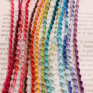 May include: A collection of 20 colorful, twisted cords of various shades of red, orange, yellow, green, blue, and purple. The cords are arranged in a rainbow pattern and are lying on a white surface.