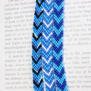 May include: Three friendship bracelets with chevron patterns in shades of blue, white, and black.