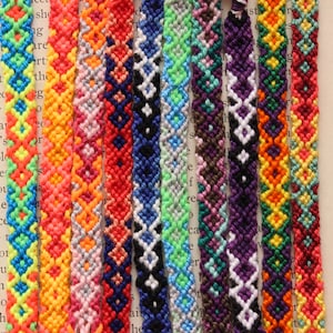 May include: A collection of colorful friendship bracelets with geometric patterns. The bracelets are made with different colored threads and feature a variety of designs.